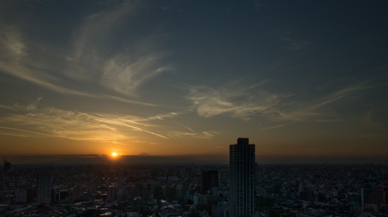 The sun is setting just to the  left of Mt. Fuji.